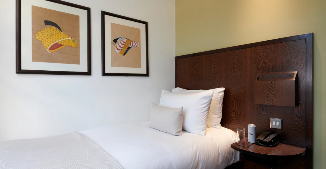 Standard Single room with a single bed, dark wood headboard and two framed prints