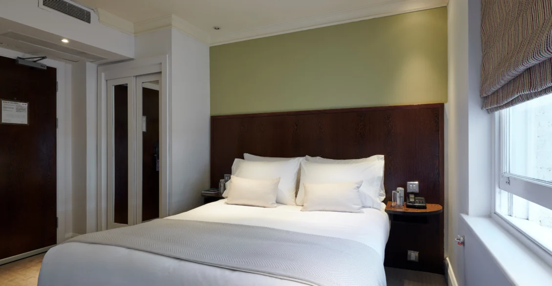 Standard Double room with a double bed and dark wood headboard beside a window