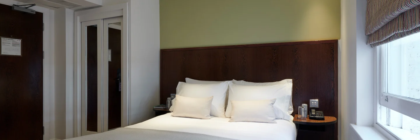 Standard Double room with a double bed and dark wood headboard beside a window