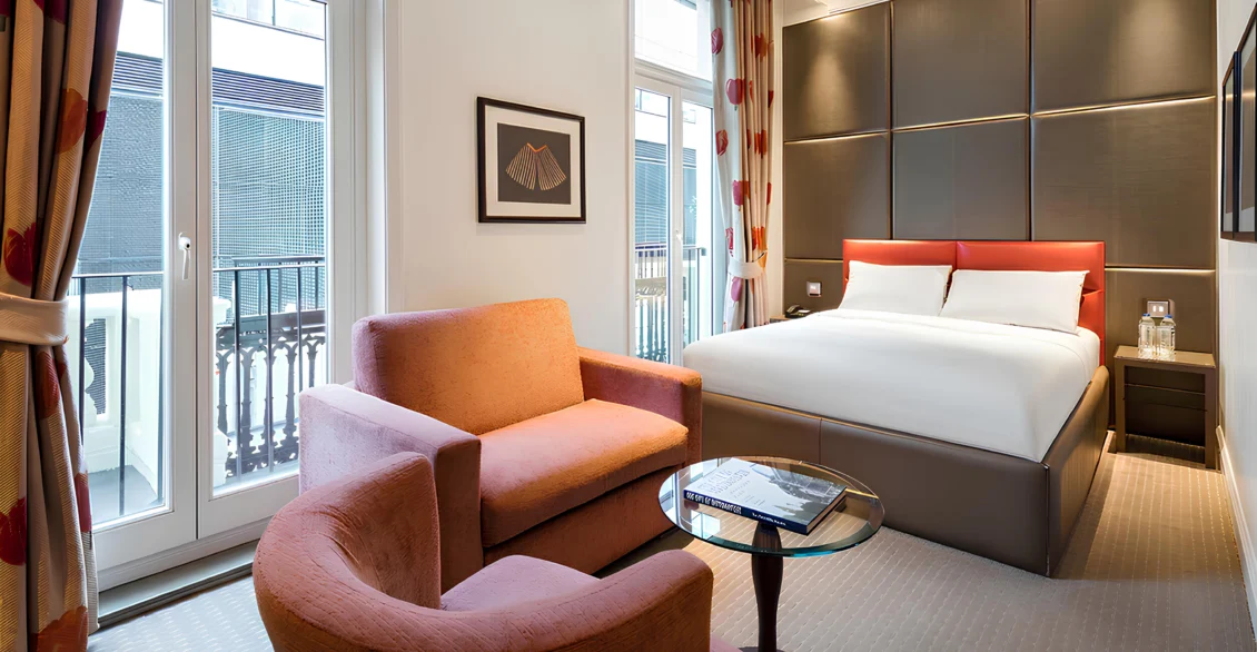 Premium King Deluxe room with orange armchairs, glass table and a king bed by French windows