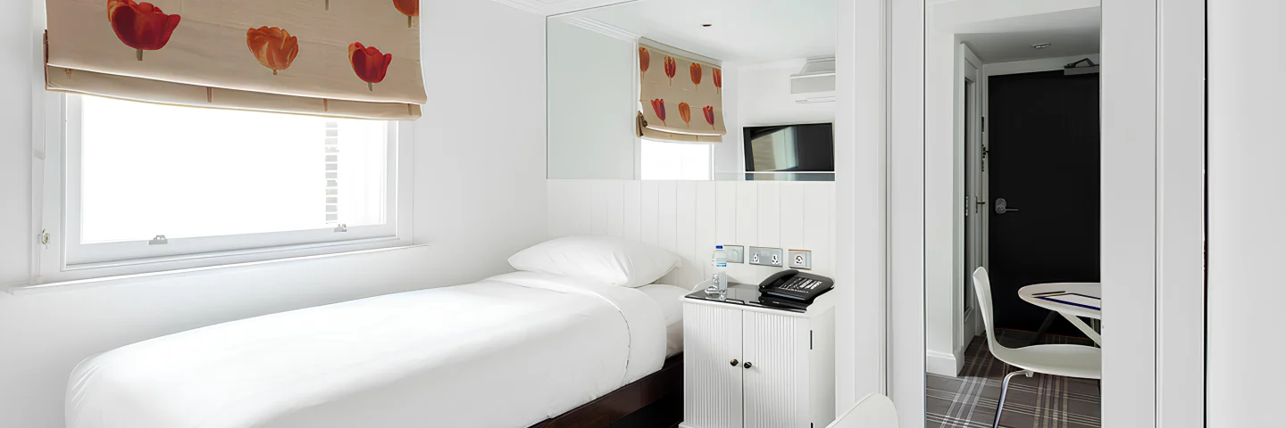 Single room with a single bed, poppy-print blinds and desk