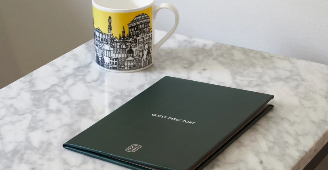 Guild Hotels London mug and a green guest directory on a marble table