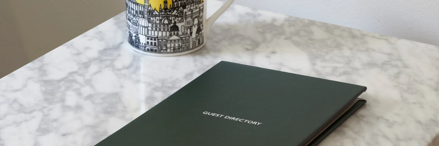 Guild Hotels London mug and a green guest directory on a marble table