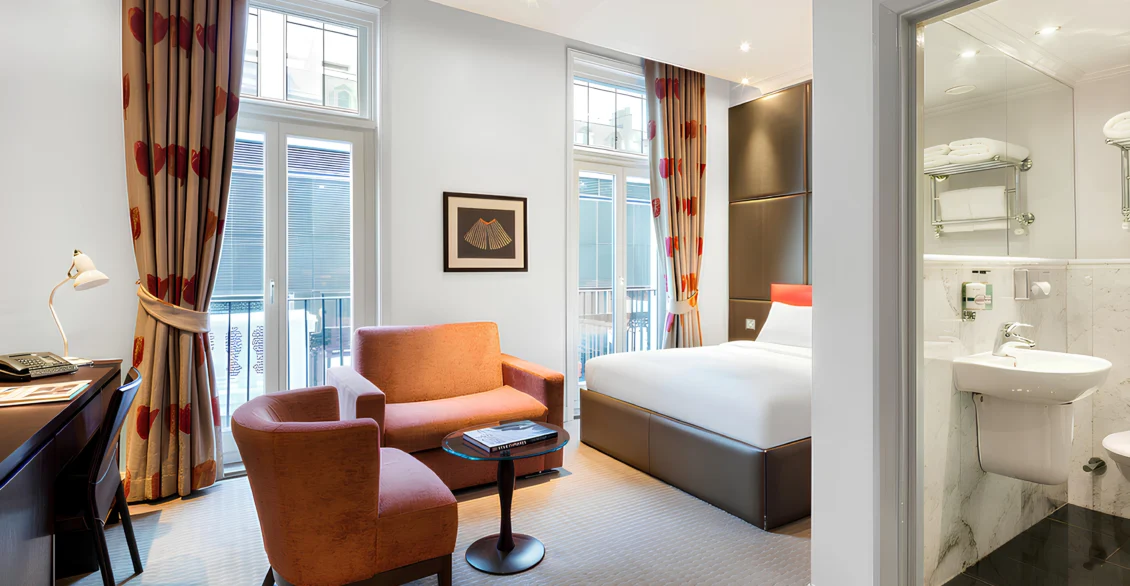 Premium King Deluxe room with orange armchairs, bed and glass-walled bathroom