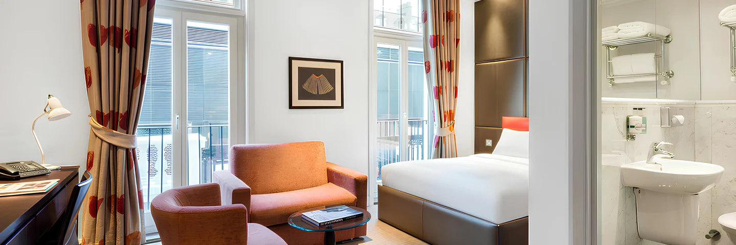 Premium King Deluxe room with orange armchairs, bed and glass-walled bathroom
