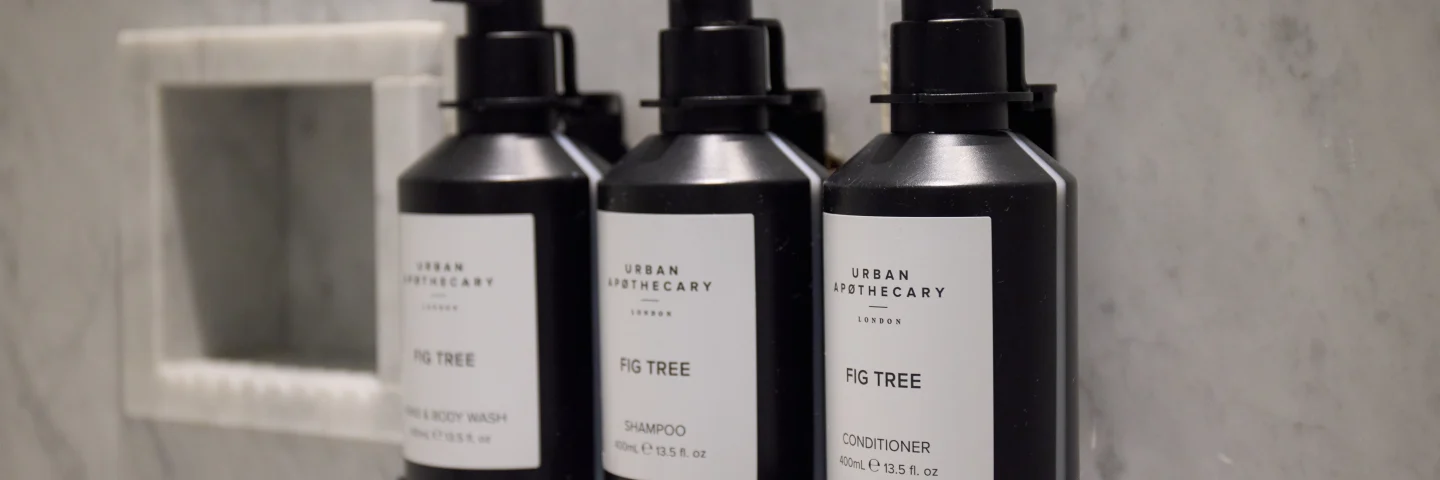 Three black toiletry bottles in a marble bathroom niche