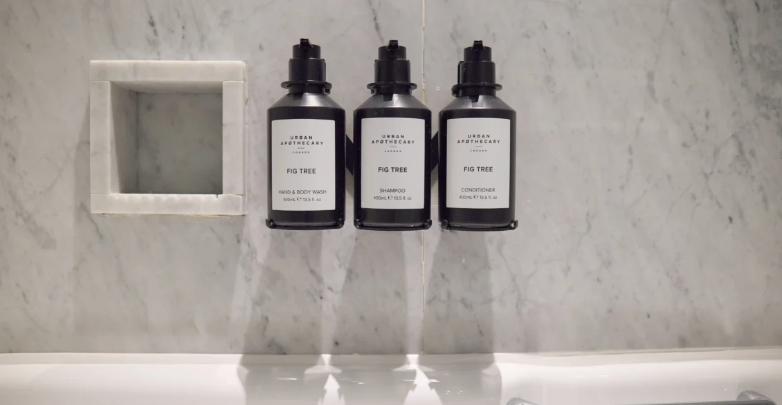 Three black toiletry bottles in a marble bathroom niche