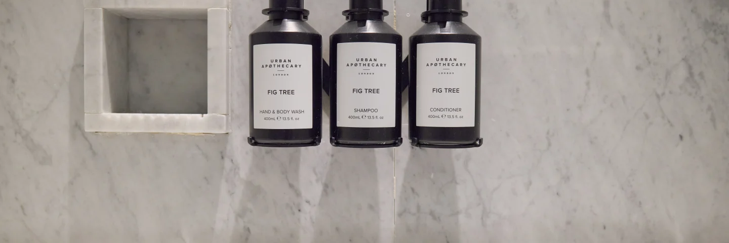Three black toiletry bottles in a marble bathroom niche