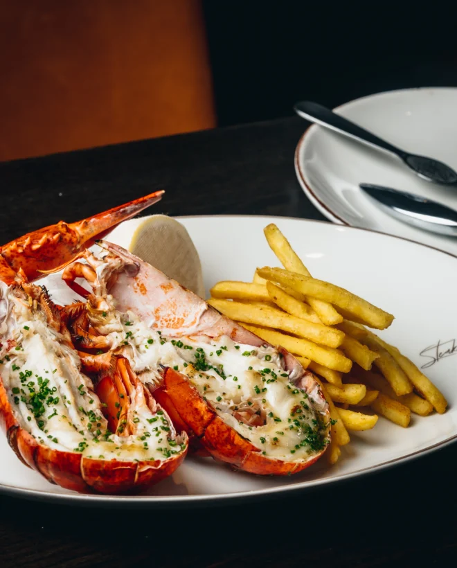 Grilled lobster with garlic butter and fries on a white plate at Steak & Lobster