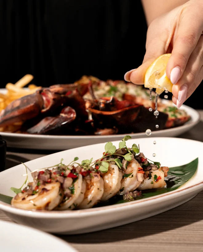 Lemon being squeezed over a grilled dish at Steak & Lobster
