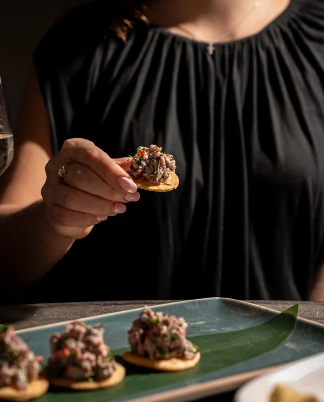 Guest lifting a steak tartare canapé from a slate serving plate