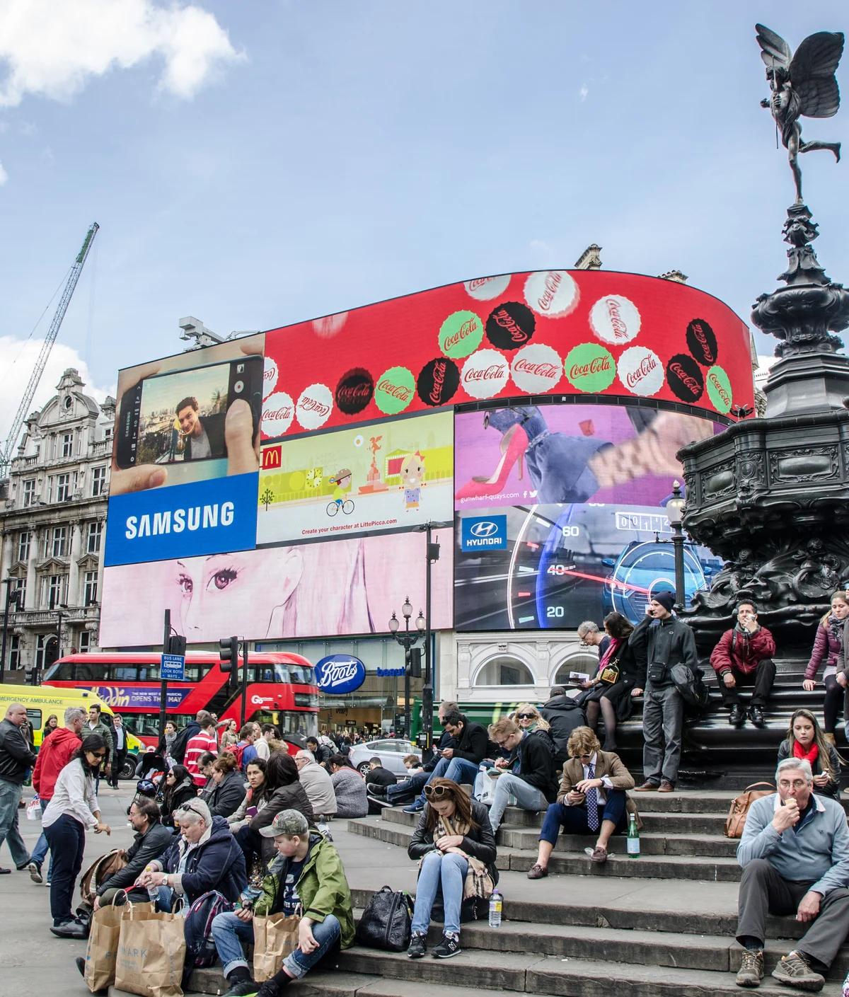 People crossing street and sit on steps of monument at Piccadilly Circus Street in London during daytime