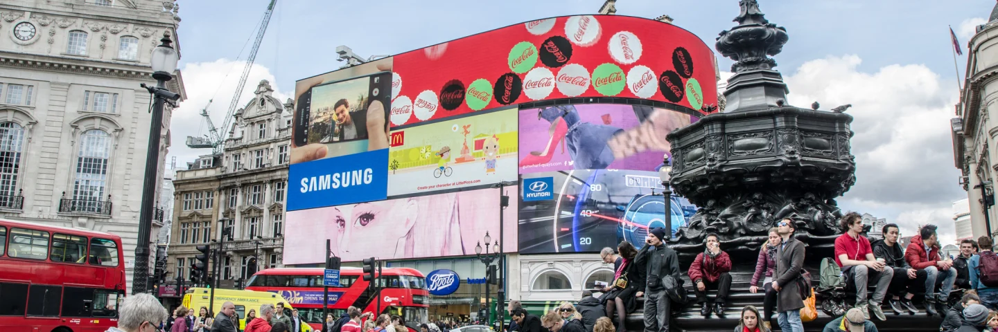 People crossing street and sit on steps of monument at Piccadilly Circus Street in London during daytime
