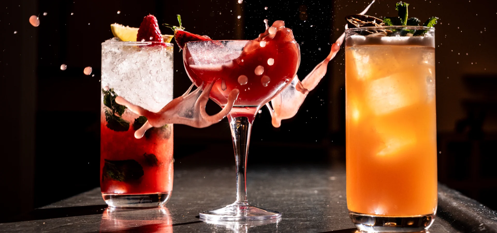 Two colourful cocktails on a bar with a splash of garnish