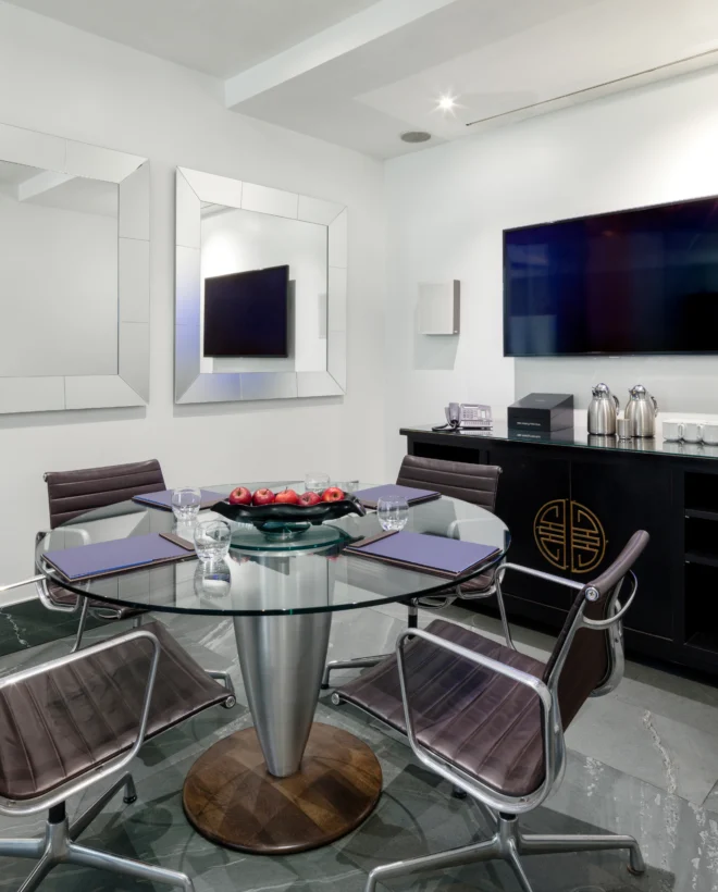 Meeting room with a round glass table, leather chairs and two wall-mounted screens