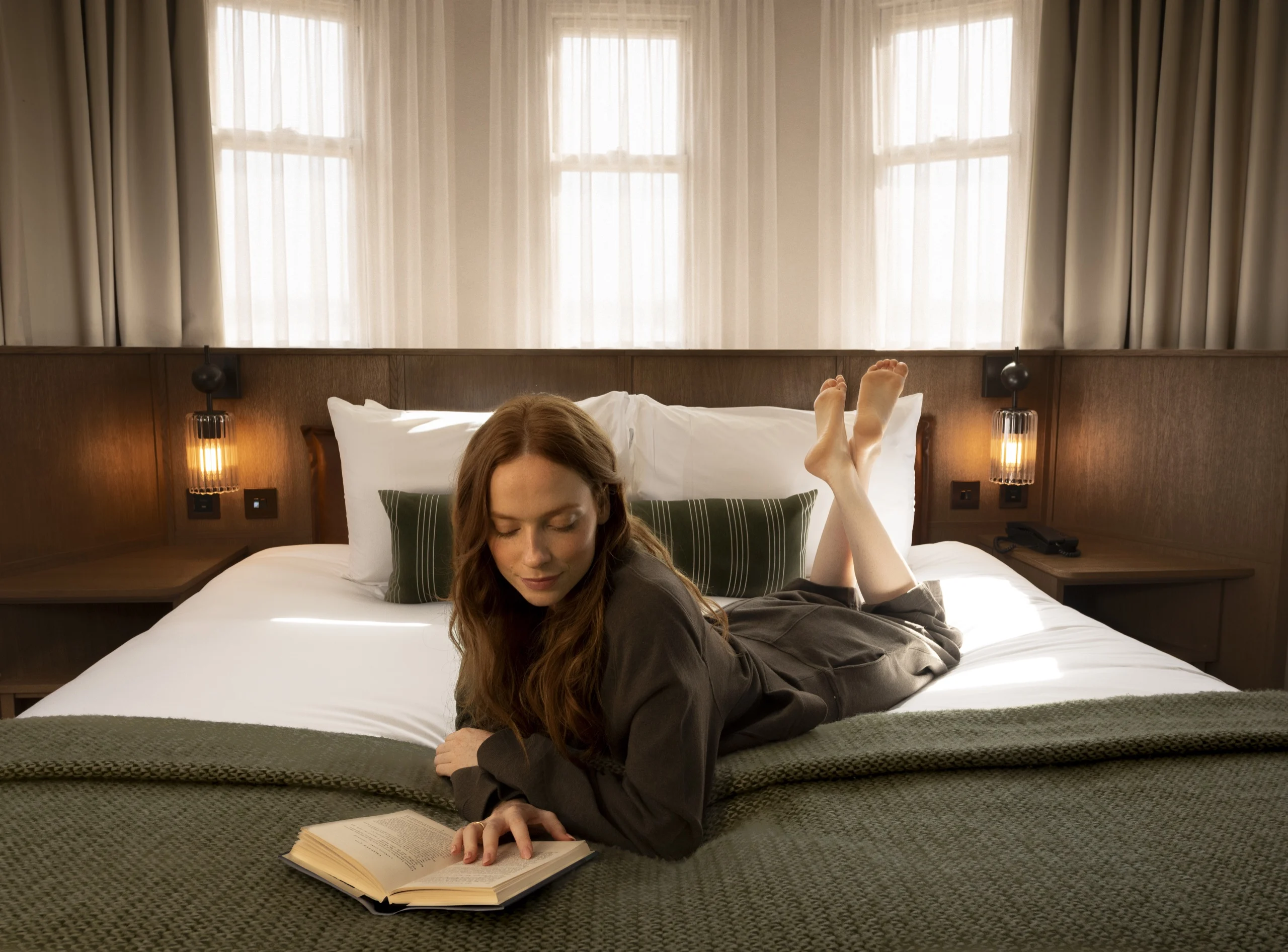 Woman reading a book on a bed in a Guild Hotel Bloomsbury suite