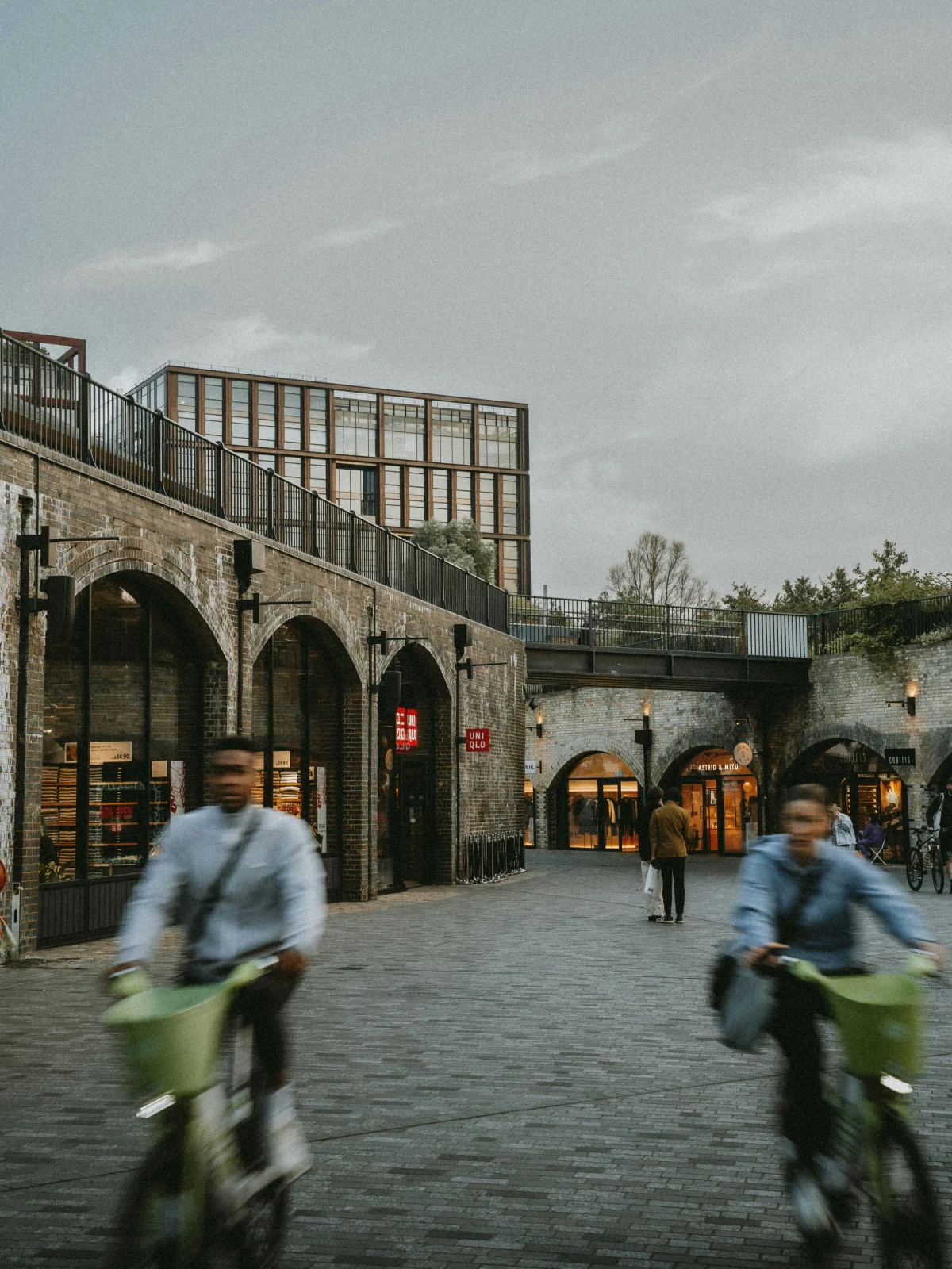 Cyclists passing the brick arches and shops of Coal Drops Yard