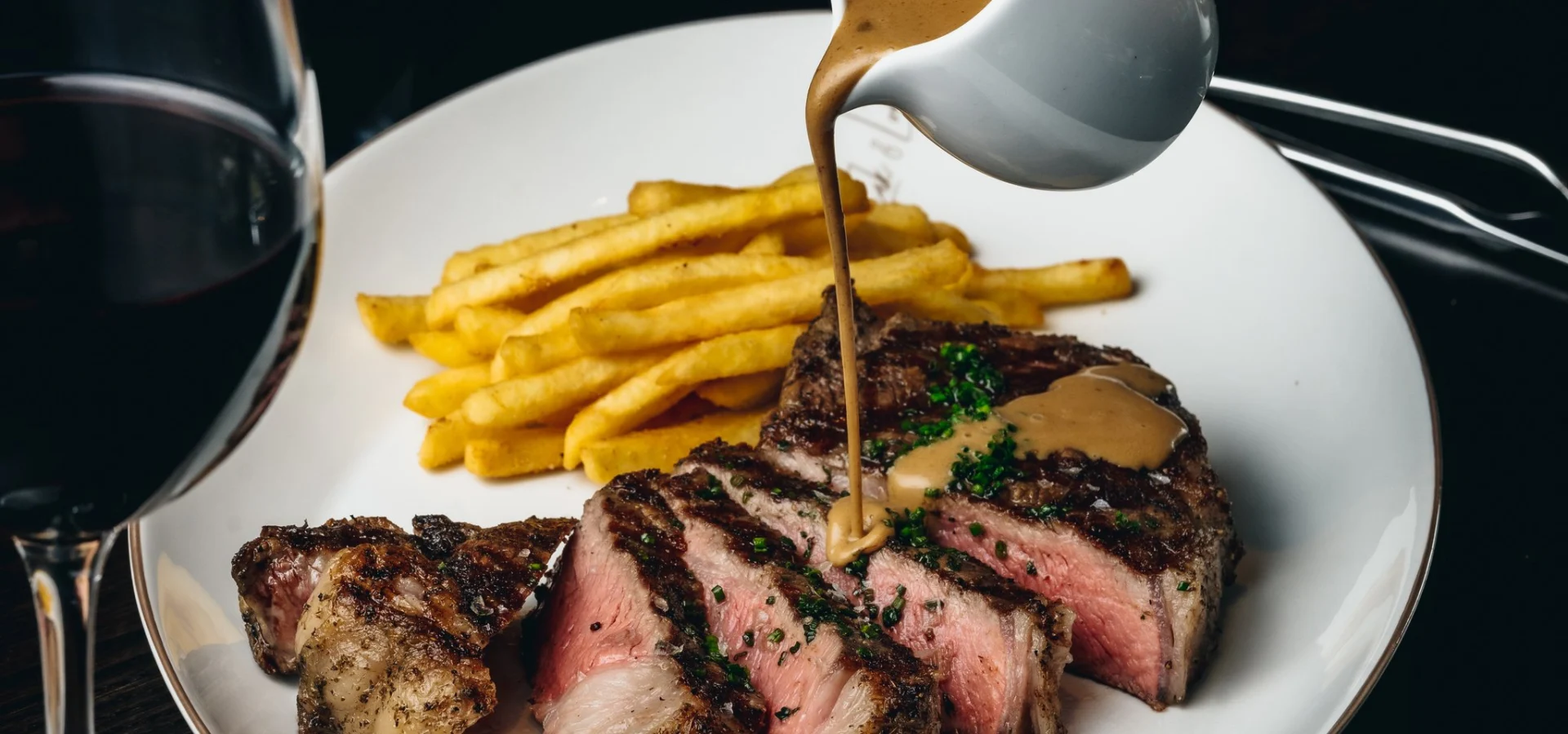 Sauce poured over sliced steak with fries and red wine