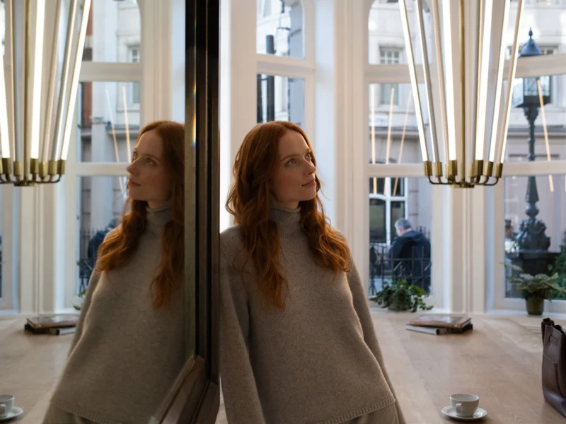 Guest leaning against a mirrored pillar beside the bay window of the Bloomsbury Street Lounge, brass pendant lights above