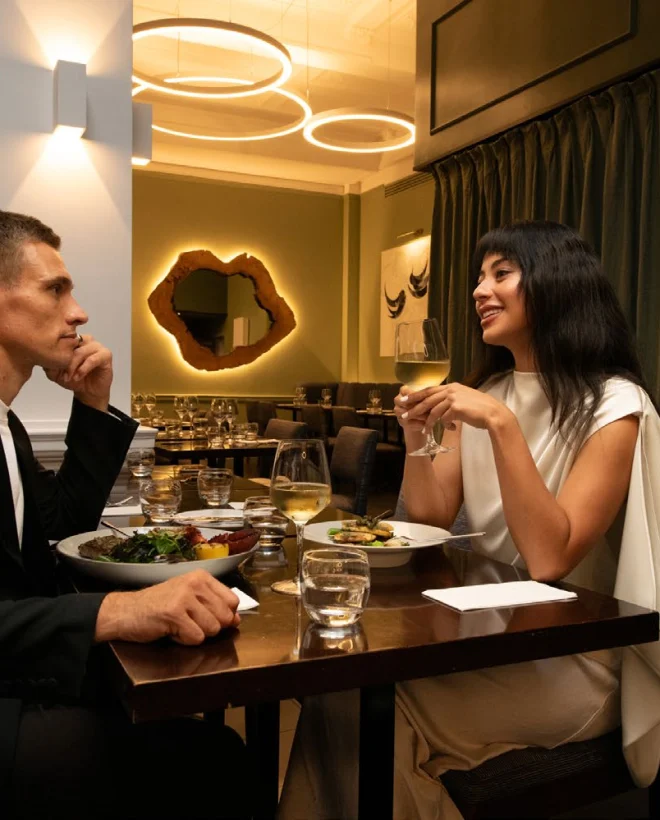 Couple dining at a wooden table in the Fitzrovia restaurant, green walls and ring pendant lights