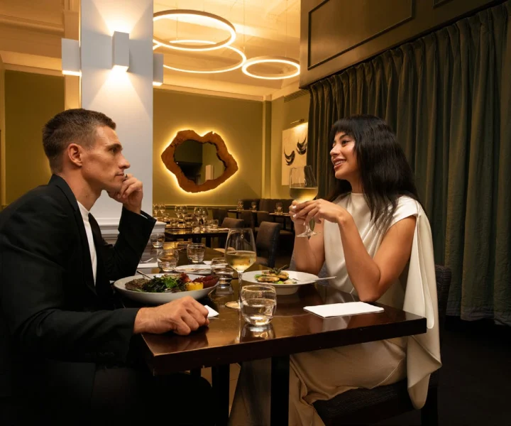 Couple dining at a wooden table in the Fitzrovia restaurant, green walls and ring pendant lights