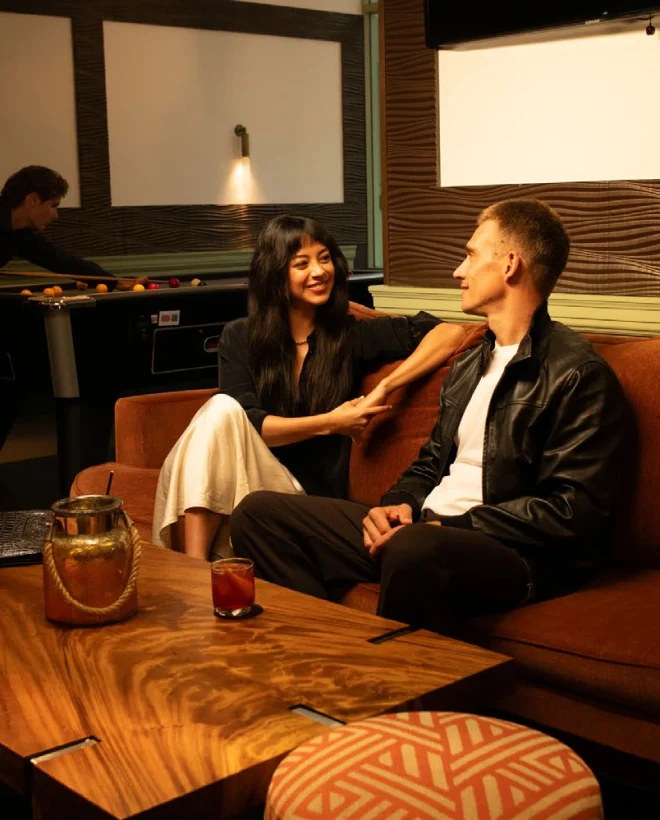 Couple on a rust velvet sofa in The Warren, pool table and sports screens behind